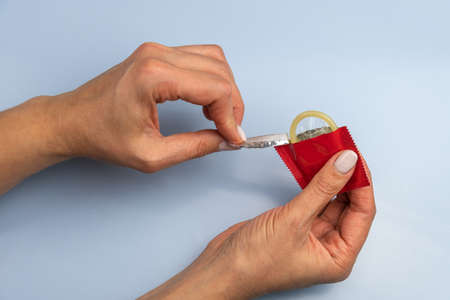 Woman opens condom on blue background close up