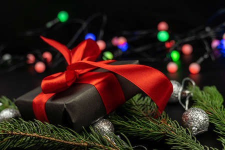 The gift box lies on fir branches decorated with New Year's toys on a black background. Christmas,...