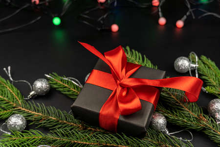 The gift box lies on fir branches decorated with New Year's toys on a black background. Christmas,...