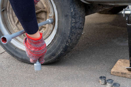 A woman with a wheel wrench unscrews a wheel from a car to replace it. Car repairの写真素材