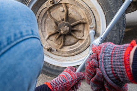 A woman with a wheel wrench unscrews a wheel from a car to replace it. Car repairの写真素材