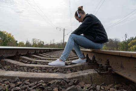 A woman sits on the tracks with headphones, listens to music. Autumn landscape