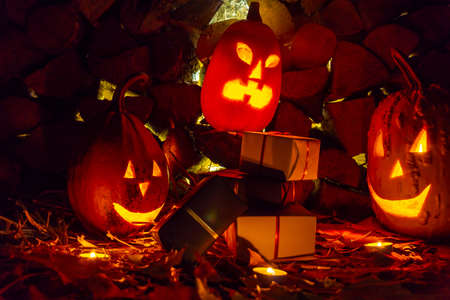 Three glowing pumpkins and a bunch of black and white gifts on fall foliage with candles on...