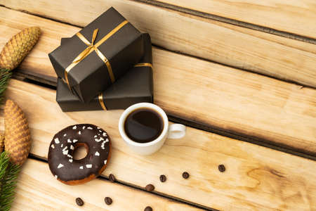 Chocolate donut, a cup of coffee and gifts in black packaging on a wooden background. New Year...
