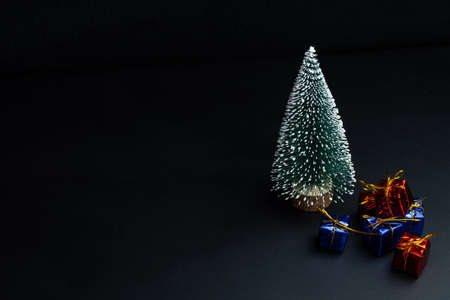 Artificial fir tree and colorful gifts on a black background, free space for text. Copy space. Merry...