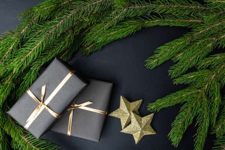 Gifts in black packaging two gold stars and fir branches on a black background. Merry Christmas and...