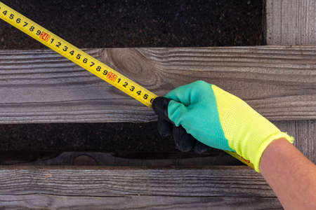 Gloved hands measure a wooden board with a tape measure. Construction and repairの写真素材