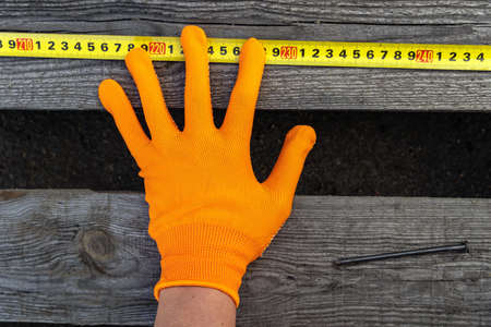 Gloved hands measure a wooden board with a tape measure. Construction and repairの写真素材