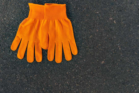A pair of orange labor gloves lie on an asphalous background