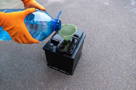 Mechanic adds electrolyte from a canister to the battery, diagnostics and repair of a car battery