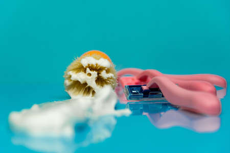 Close-up of a shaving brush focus on the middle of the shaving brush with shaving foam and a pink razor on a blue background. In the foreground, the shaving foam is out of focus.の写真素材