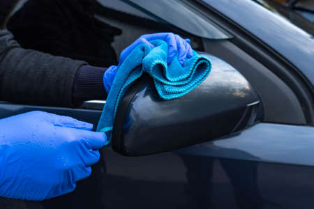A woman's hand in a blue glove washes the car mirror with a blue rag. Car care and washingの写真素材