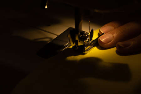 Image of a seamstress working on a sewing machine at night. Women's hands on the sewing machine. Shallow depth of field.の写真素材