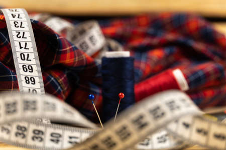 A close-up of a pin against the background of a cut of fabric in a cage of two skeins of thread, in the foreground a centimeter tape out of focus. Shallow depth of fieldの写真素材