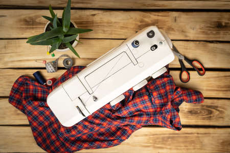 White sewing machine, which sews a plaid men's shirt. Cutting and sewing concept. Women's hobby