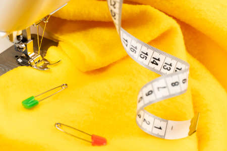 A piece of yellow cloth on a sewing machine and a centimeter. The fabric under the sewing machine...