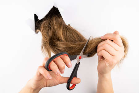 The girl cuts her hair with scissors through the hole in the wall. Self-care concept, haircut.の写真素材