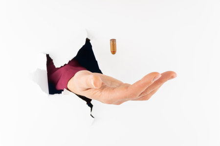 The cartridge of the pistol hovers in flight towards the hand  who is looking through a hole in a...