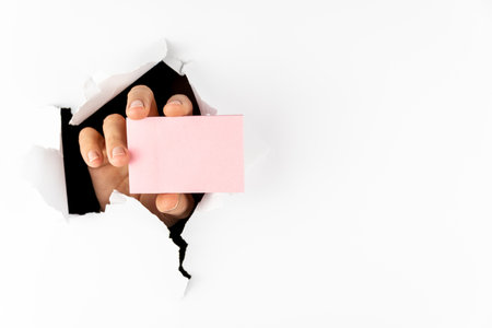 A woman's hand holds a paper notebook through a hole in a white wall. Free space for textの写真素材