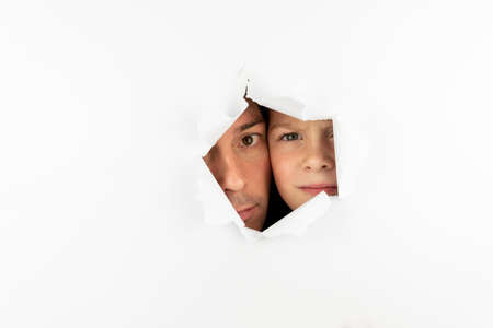 The boy looks through a hole in the white wall. Free space for textの写真素材