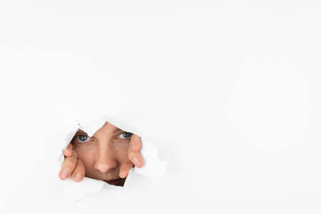 A woman looks through a hole in the paper, pushing her hands apart. Independence and freedom conceptの写真素材