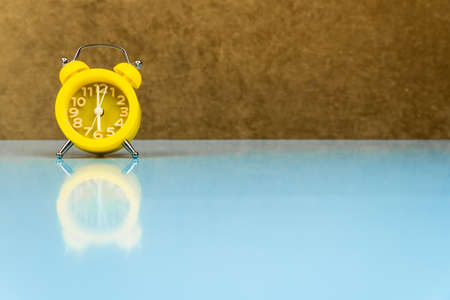 Yellow alarm clock on a blue table and brown background. Time and mood concept. Free space for textの写真素材
