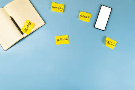 Scatter yellow stickers with the words Blue Monday, a notebook and a smartphone on the blue table....