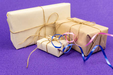 Gifts wrapped in white paper and tied with burlap rope, and colorful ribbons on a purple background....