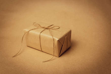 The gift is wrapped in yellowed paper and tied with burlap rope on a beige background. Retro photography. Free space for entering textの写真素材