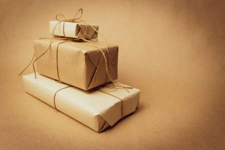 The gifts are wrapped in white paper and tied with burlap rope, folded into a herringbone on a beige background. Retro photography. Free space for entering textの写真素材
