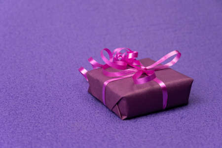 Gift on a violet background. The box is wrapped in purple paper and tied with pink tape. Free space...