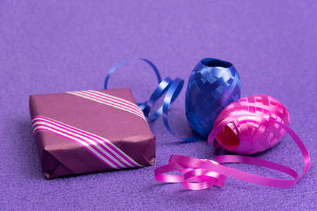 Gift in a violet box and a decorative ribbon next to a violet background New Year's background