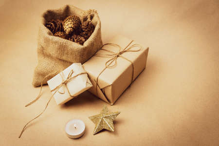Handmade Christmas boxes wrapped in kraft paper and a decorative bag with pine cones on a beige...