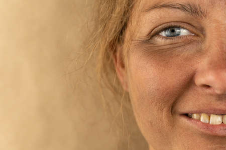 Close-up of half of the face of a homeless girl who smiles on a brown background. Free space for textの写真素材