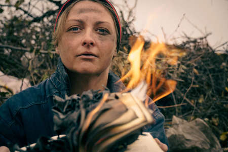 Close-up of a female dirty face through a burning book. Homeless woman sets fire to a book in a...