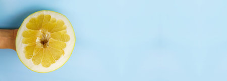 Pomelo half in hand on a blue background close-up. Free space for textの写真素材