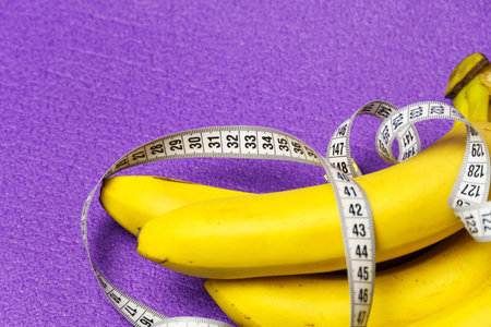 Close-up of a bunch of bananas and a measuring tape on a purple background. Healthy lifestyle and proper nutrition.の写真素材