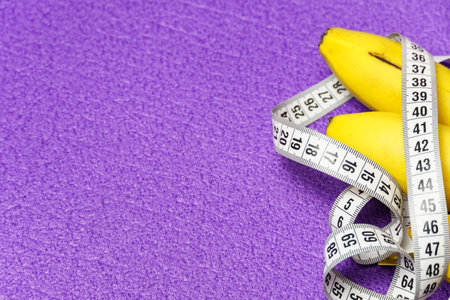 Close-up of a bunch of bananas and a measuring tape on a purple background. Healthy lifestyle and...