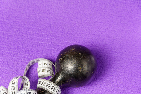 Old black rusty dumbbells and a white measuring tape on a purple background. Copy space. Sport and...