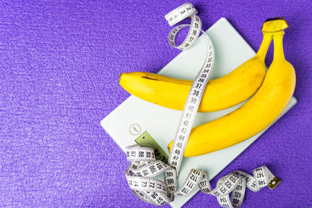 On the electronic scale are two bananas and a measuring tape on a purple background. Healthy lifestyle and proper nutritionの写真素材