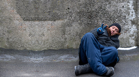The homeless man, leaning on his elbow, lies and shows a sign of victory on his fingers. Free space for text.の写真素材