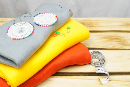 Multicolored fabrics and pins on wood background.Sewing background