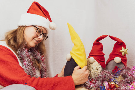 The girl is playing with homemade Christmas gnomes. A girl of 30-35 years old wearing a Santa Claus hat. Handmade Scandinavian gnomes. Christmas moodの写真素材
