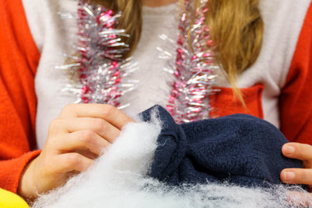 The girl sews a New Year's gnome. Close-up of female hands stuffing a toy with padding polyester....