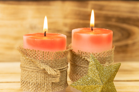 Christmas candles on wooden background, shallow depth of field. Two red candles are wrapped in a sack rope, next to a shining Christmas star. Christmas backgroundの写真素材