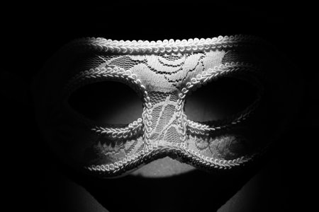 White festive carnival mask in the shadow of a point light on a black background. Mystery and mysticism conceptの写真素材