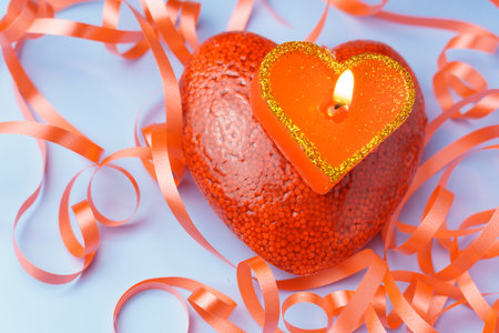 A candle in the shape of a red heart stands on a red heart on a blue background in a serpentine. Human burning love conceptの写真素材