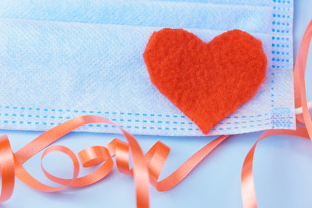 Close-up of a blue medical mask on a blue background with a red heart and serpentine. Pandemic love conceptの写真素材