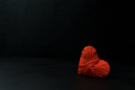Heart on a black background. Homemade heart made of red threads. Valentine's day, romance and loveの写真素材