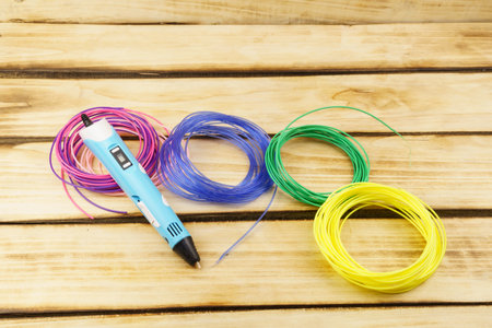Multicolored plastic threads and 3d pen on a wooden background. Creativity conceptの写真素材